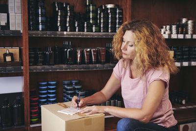 Saleswoman writing on paper by rack in deli