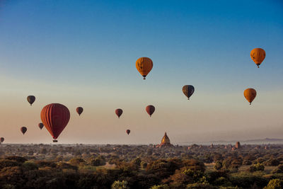 Hot air balloons flying over landscape against clear sky during sunset