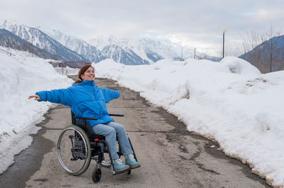 A woman in a wheelchair spread her arms to the side like wings in the mountains in winter