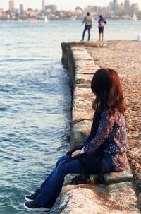 Rear view of woman sitting on beach looking at sea