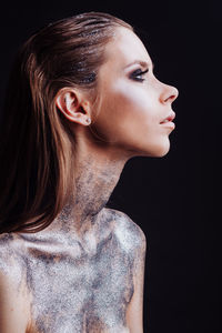 Close-up of young woman with silver bodypaint over black background