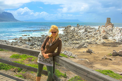 Portrait of mature woman wearing sunglasses standing by railing against sea