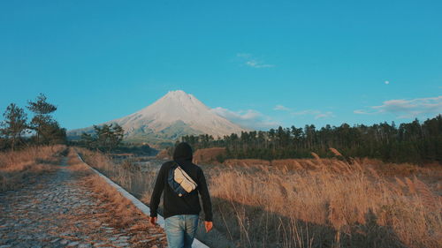 Rear view of man walking by field on road