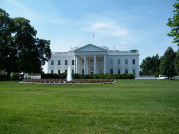 Lawn in front of white house against sky