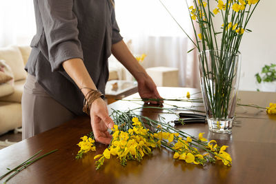 Midsection of woman holding flower vase on table