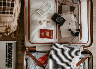 Open baggage with snickers, sweater, laptop, headphones and passport, vintage camera and backpack.