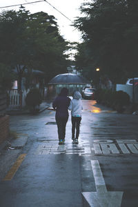 Rear view of mother and daughter walking with umbrella on wet street