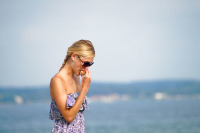 Young woman eating fruit against sea