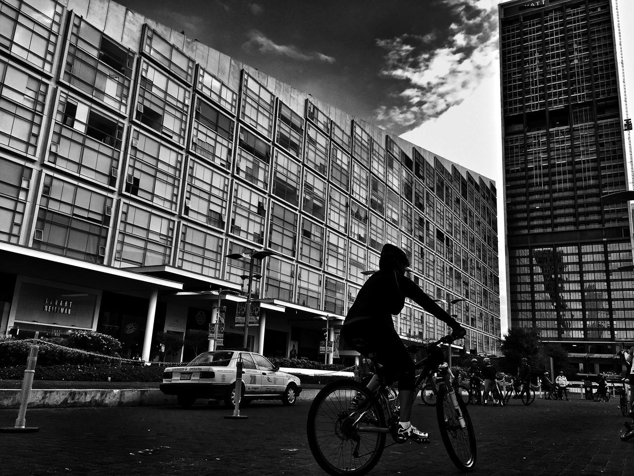 architecture, transportation, bicycle, built structure, building exterior, mode of transport, full length, city, men, on the move, land vehicle, riding, city life, leisure activity, cycling, sky, lifestyles, travel, office building, outdoors, cloud - sky, day, tall - high