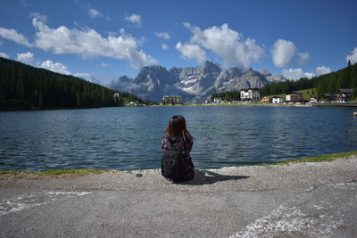 Rear view of woman sitting by lake against sky