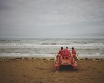 Men sitting on lifeboat at beach against sky