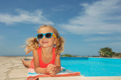 Portrait of woman wearing sunglasses while sitting in swimming pool against sky