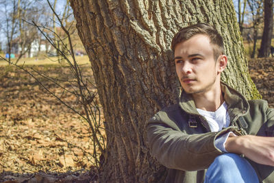 Handsome man sitting against tree trunk at park