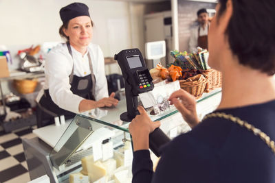 Saleswoman looking at female customer entering pin in credit card reader at grocery store