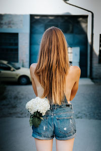 Rear view of woman with flowers in pocket standing on road