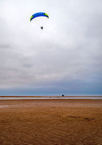 Person paragliding on beach against sky