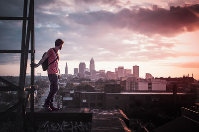 Full length of man standing by cityscape against sky during sunset