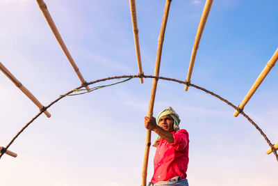 Low angle view of fisherman standing against sky during sunset