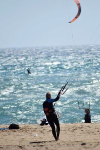 Rear view of men fishing in sea against clear sky