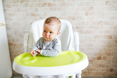 Cute baby girl holding spoon on high chair at home