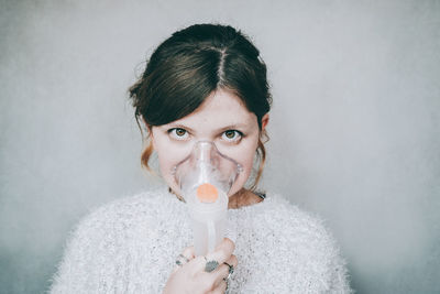 Portrait of woman breathing with oxygen mask against wall