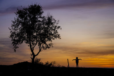 Silhouette man standing by tree against sky during sunset