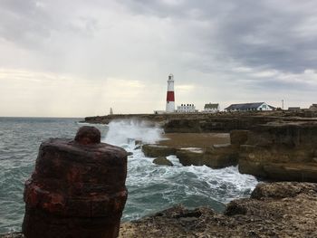 Lighthouse on beach by sea against sky