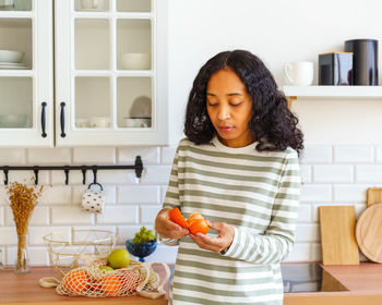 African-american female checking orange citrus for spoilage in kitchen after grocery shopping