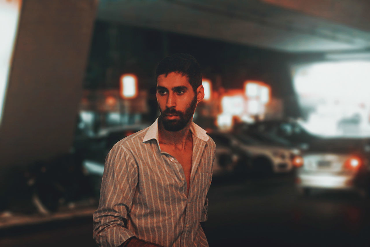 one person, adult, portrait, men, young adult, looking at camera, beard, standing, transportation, city, front view, facial hair, waist up, architecture, focus on foreground, vehicle, mode of transportation, car, casual clothing, lifestyles, street, fashion, motor vehicle, serious, night, person, looking, city life, copy space
