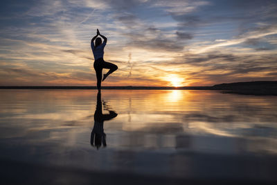 Reflection of silhouette person in sea against sky during sunset