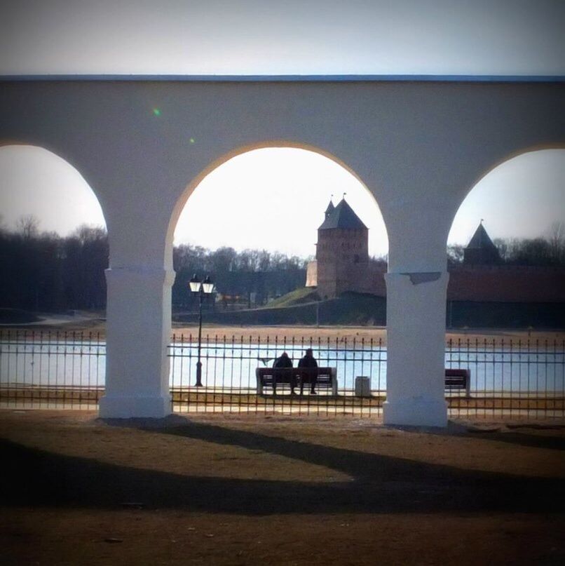 architecture, built structure, arch, men, silhouette, lifestyles, transportation, leisure activity, person, building exterior, bridge - man made structure, rear view, river, sitting, full length, walking, sky