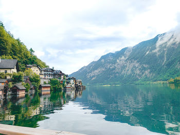 Lake by houses and mountains against sky