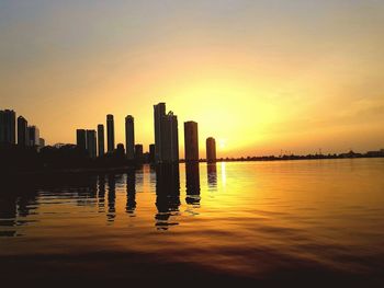 Silhouette of city at waterfront during sunset