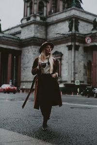 Full length of tourist with camera walking on wet road in city during rainy season