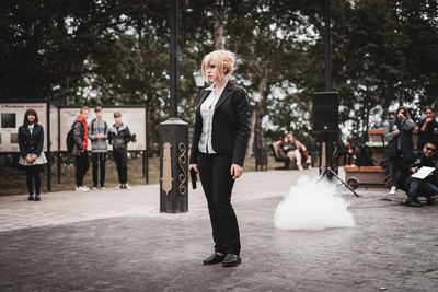 Full length portrait of woman standing on sidewalk in city