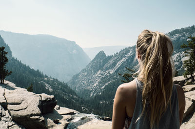 Rear view of woman standing on cliff against mountains