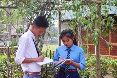 Teenage girl with friend wearing school uniforms writing on book