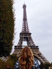 Rear view of woman standing in front of eiffel tower against sky