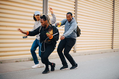 Full length of friends dancing on sidewalk by shutter in city