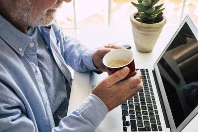 Midsection of senior man holding coffee cup sitting at office