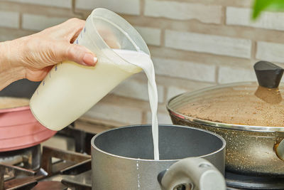 Woman pours milk from jug into pan for making cream pie in her home kitchen