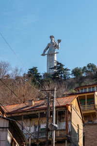 Low angle view of statue by building against blue sky