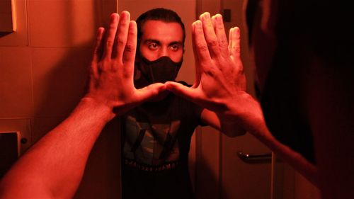 Young man wearing mask touching mirror at home