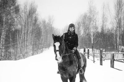 Young woman riding horse on snow covered field in forest