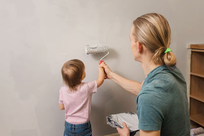 Person holding paint roller over gray wall. father with child doing decoration and re-design of room