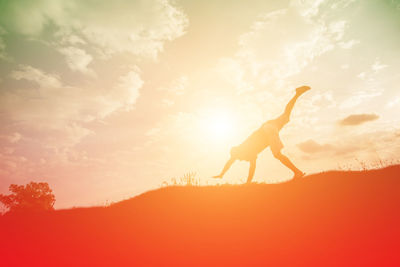 Silhouette woman with arms raised against sky during sunset