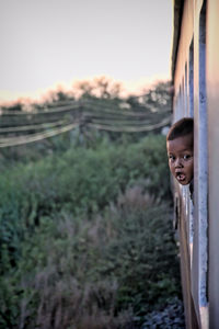 Portrait of girl standing by window against sky