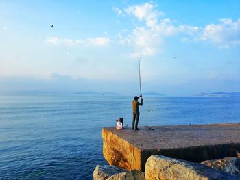 Rear view of man fishing on pier by sea against sky