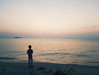 Rear view of boy standing on beach against clear sky