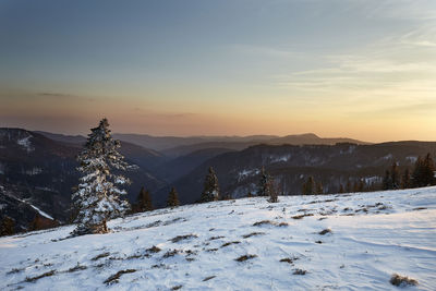 Snow covered landscape against sky during sunset